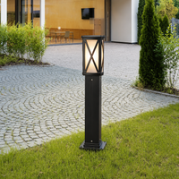 Modern black aluminum X brace grid bollard light on green grass lawn edge next to cobblestone patio driveway walkway styling.