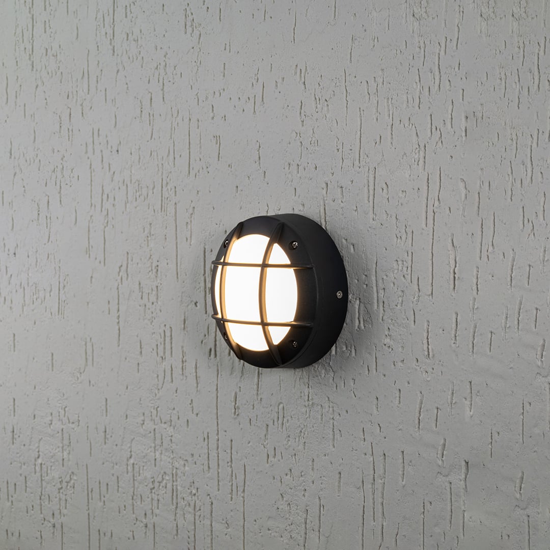 Round outdoor wall light with black metal frame and warm glow on white background for modern exterior lighting decor.