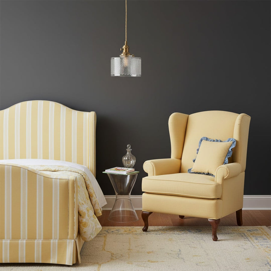 Textured clear glass and brass metal pendant light creating cozy ambience beside the armchair indoors.