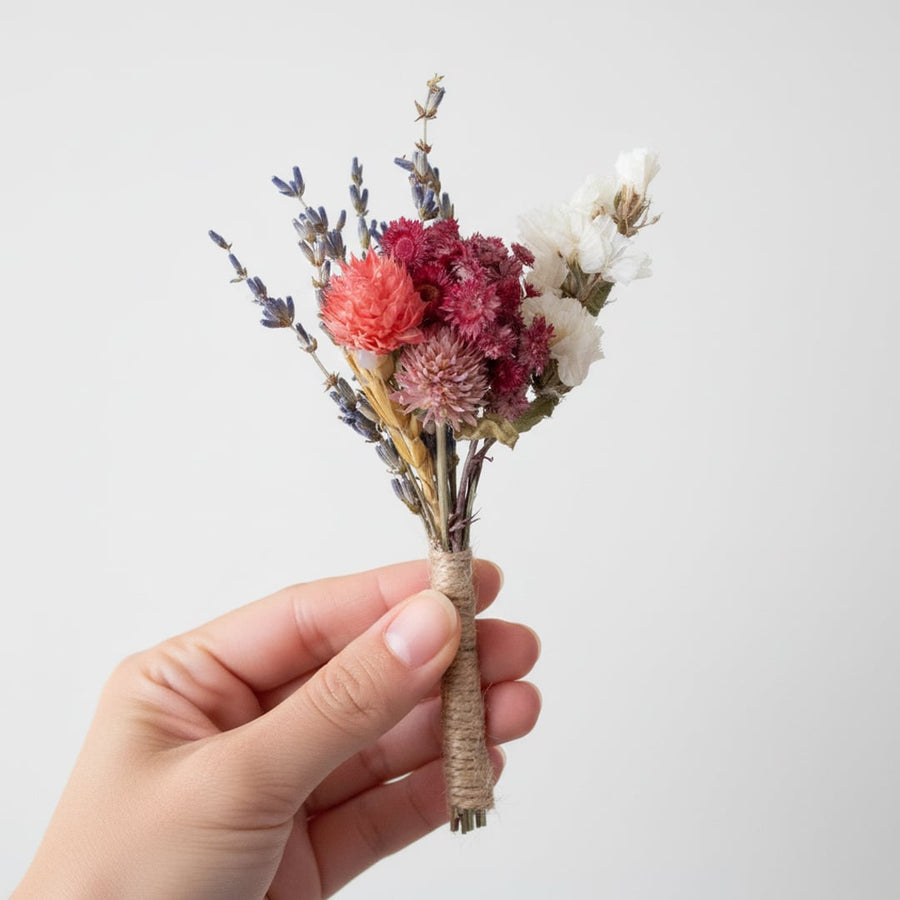 Mini dried flower bouquet with mixed preserved blooms wrapped neatly and held in hand on white background for decor accents.