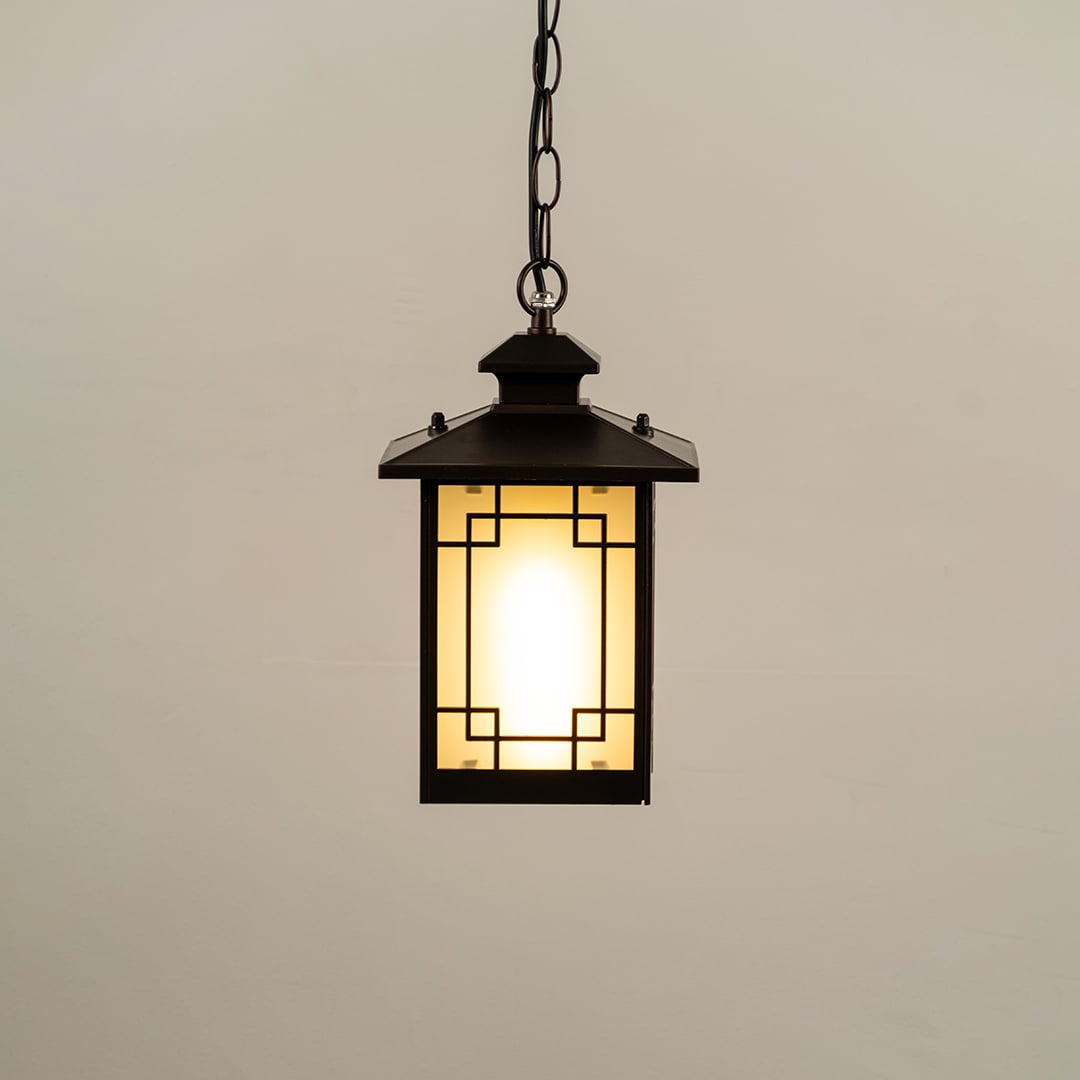 Black hanging lantern on white background with light on displaying glowing frosted glass geometric metal frame and compact design ideal for porches and patios.