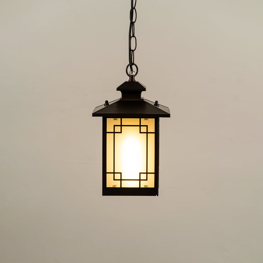 Black hanging lantern on white background with light on displaying glowing frosted glass geometric metal frame and compact design ideal for porches and patios.