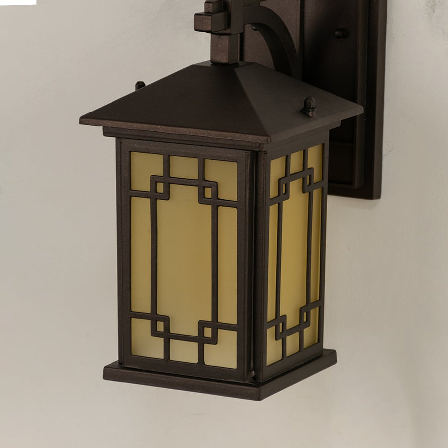 Closeup of brown outdoor metal lantern showing warm illuminated frosted glass and detailed geometric frame for elegant exterior lighting.