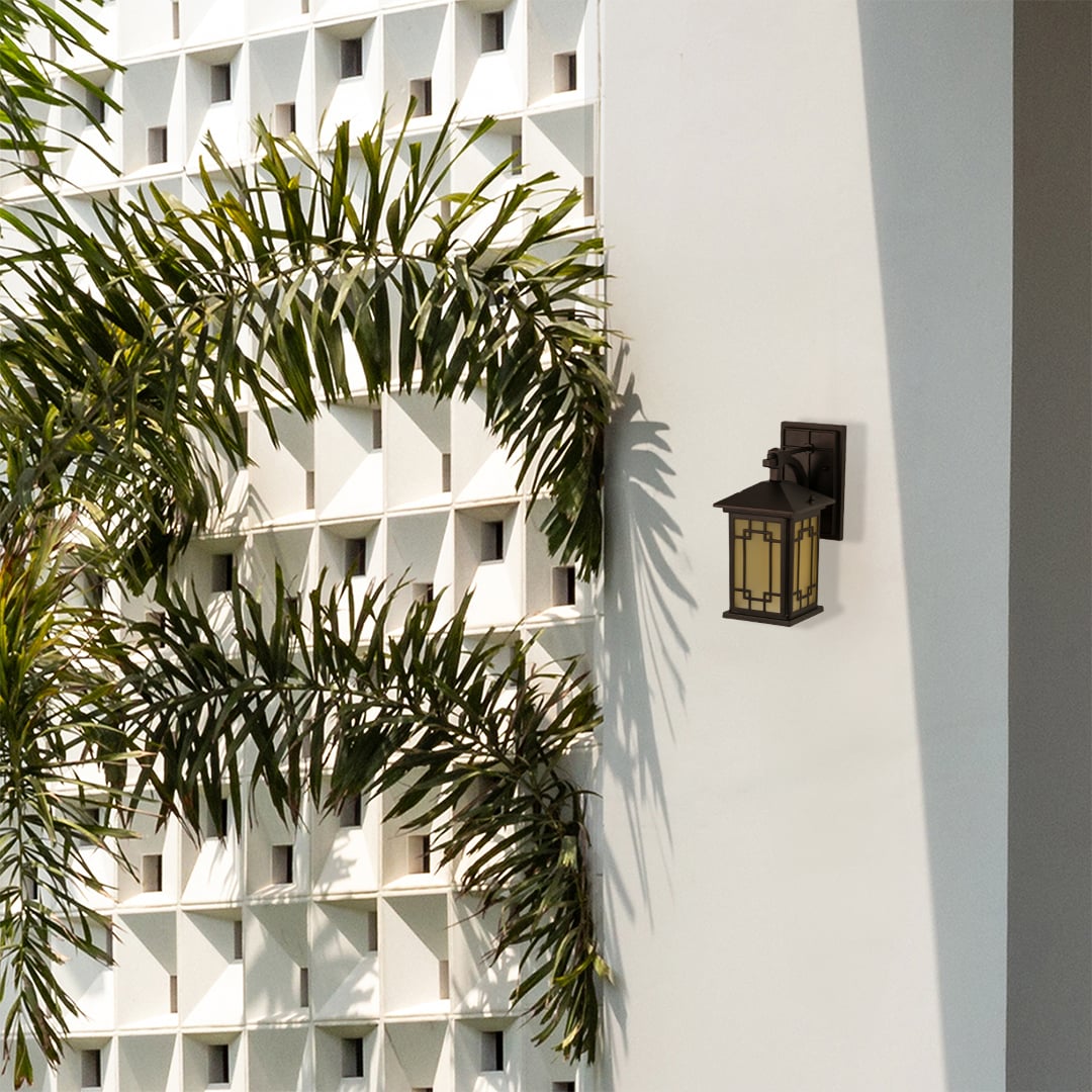 Elegant brown metal outdoor lantern with warm light on mounted on a bright exterior wall adding a soft welcoming glow to garden and patio spaces.