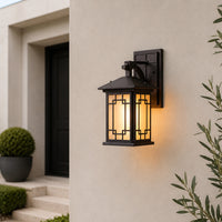 Black metal outdoor wall lantern lifestyle image with geometric lattice frosted glass shade on white exterior entryway wall.
