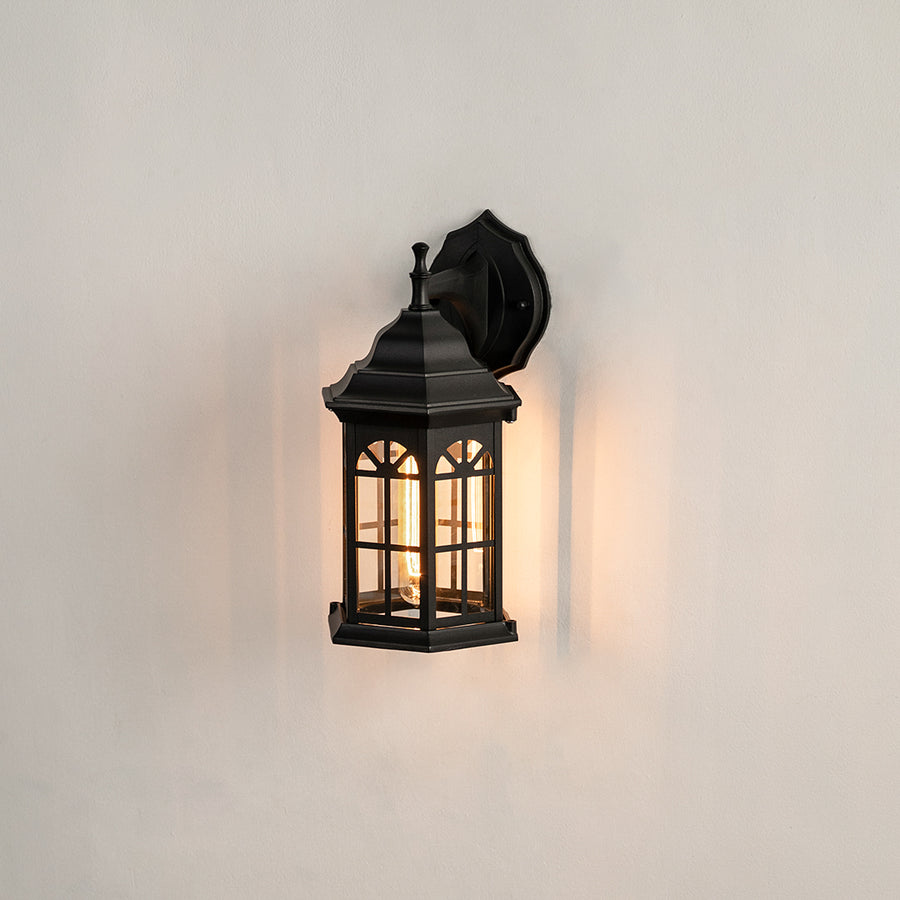 Black metal outdoor wall lantern on white background with an arched paneled glass shade for traditional patio decor.