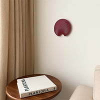 A stylish shell shaped wall decor plate in a deep maroon tone displayed in a minimal room setting adding a bold artistic accent to modern home interiors.
