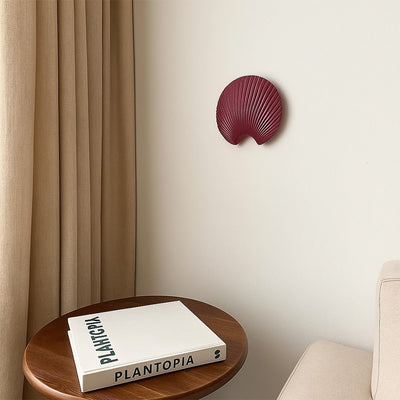 A stylish shell shaped wall decor plate in a deep maroon tone displayed in a minimal room setting adding a bold artistic accent to modern home interiors.