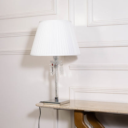 Glass lamp with lights off highlighting crystal details chrome base and pleated white shade on white background.