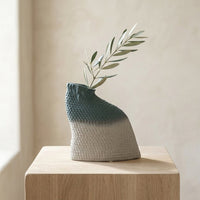 Textured grey and blue artisan vase with green leaf on pedestal for artistic modern home decor and shelf centerpiece.
