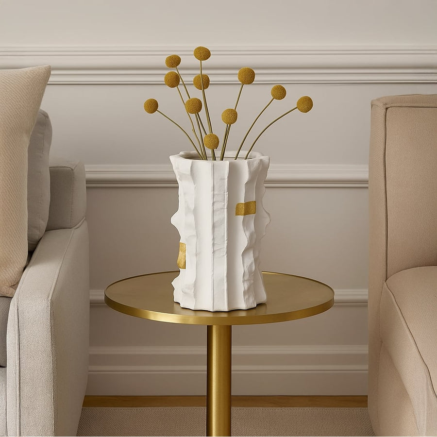 Astra white ceramic vase with gold accent details styled on a round brass table between two beige sofas adding a modern luxury touch to living room decor.