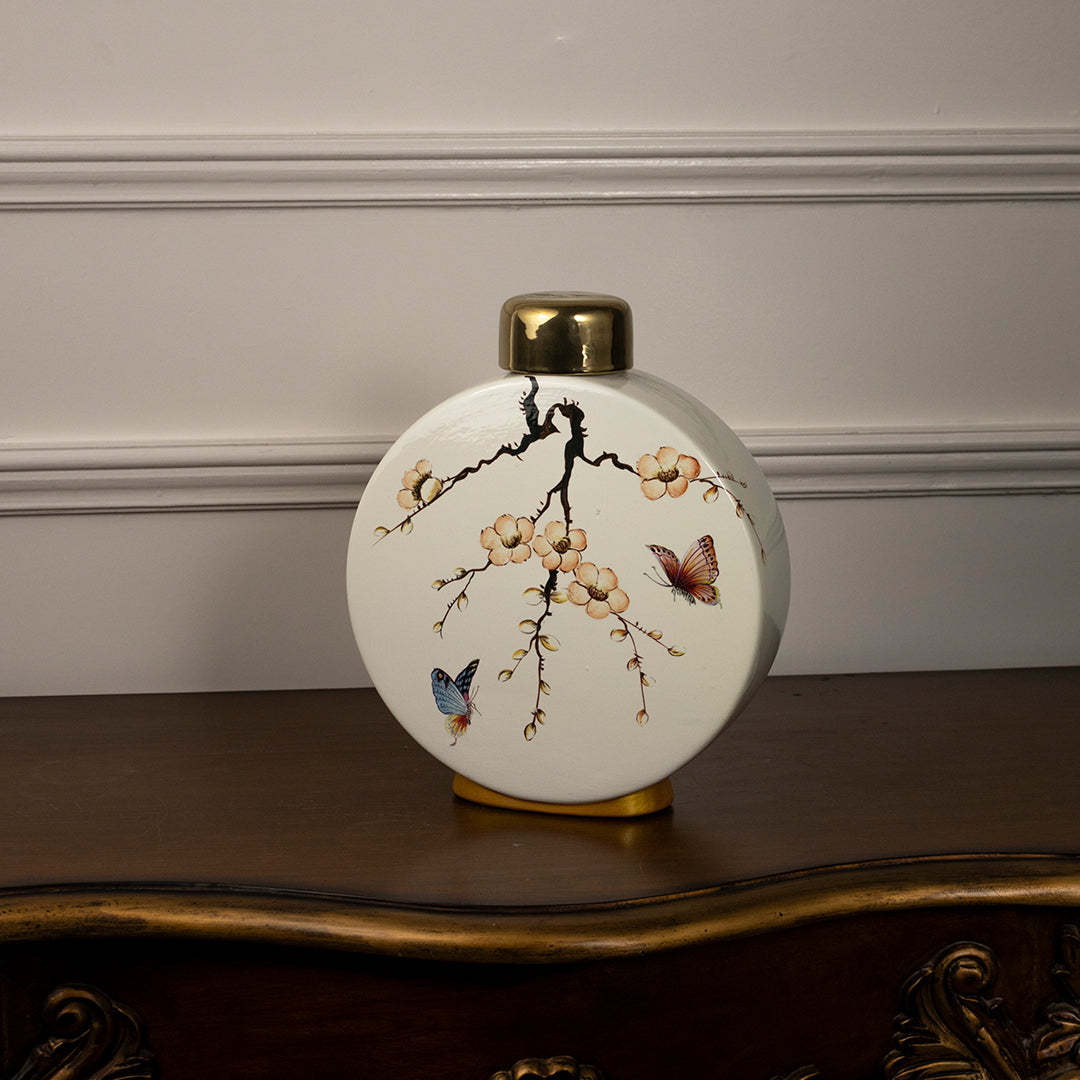 Round ceramic vase with bird and branch artwork and gold neck placed on wooden table against neutral wall background showcasing elegant decorative home styling.