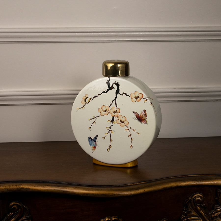 Round ceramic vase with bird and branch artwork and gold neck placed on wooden table against neutral wall background showcasing elegant decorative home styling.