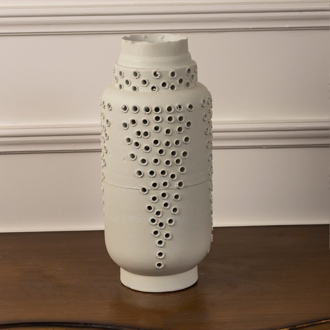 Minimalist tall white ceramic vase with perforated textured design ideal for shelf styling and modern home or office decor.