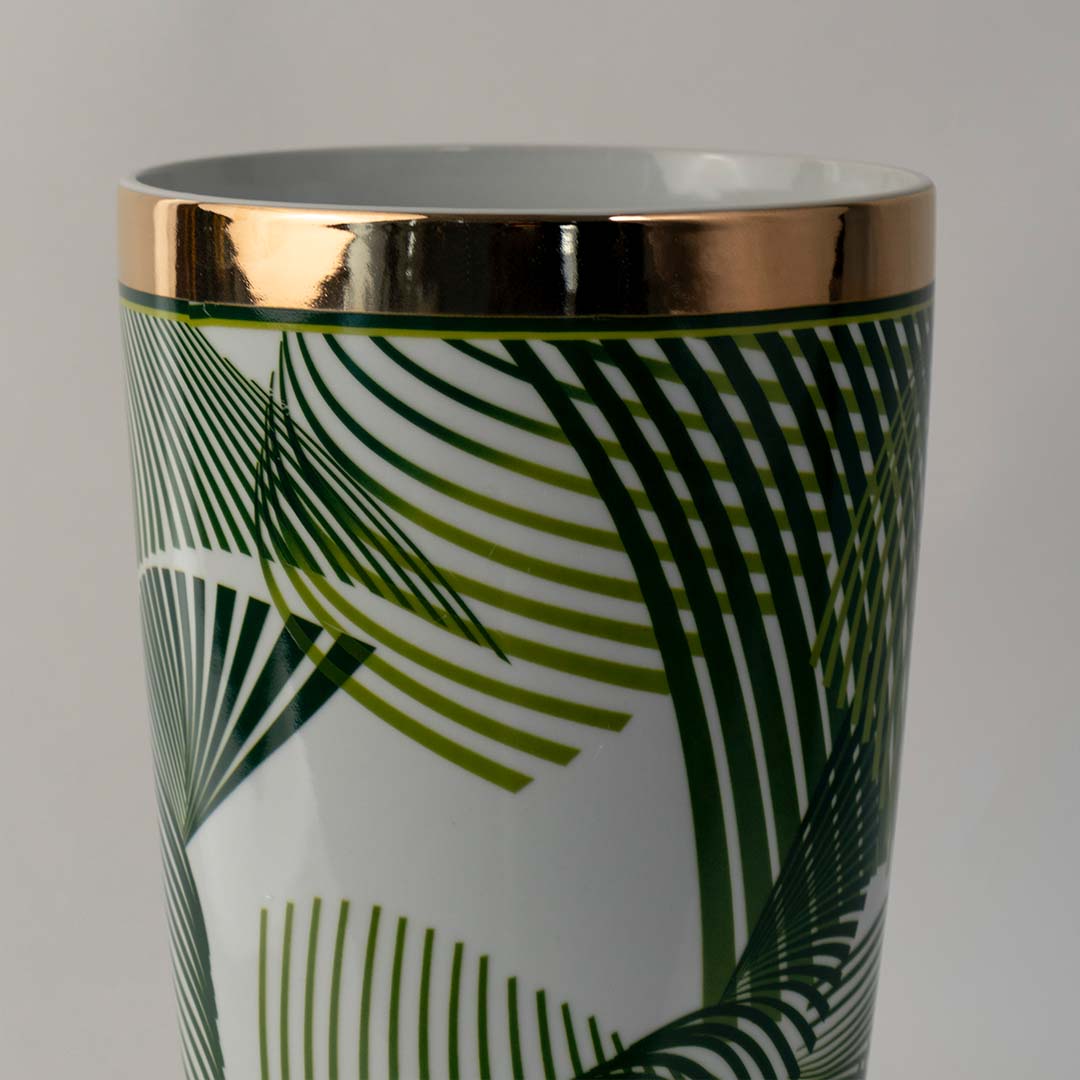 Glossy ceramic planter with green leaf pattern and gold rim placed on white surface against neutral background enhancing tropical inspired home decor styling.
