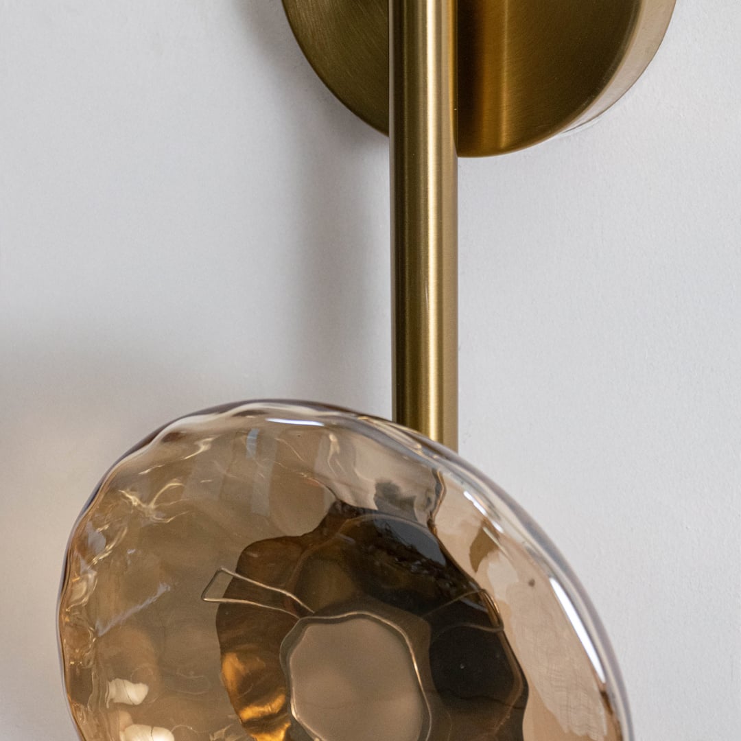 Closeup image of gold metal wall light with hammered smoked glass shade for modern decorative wall lighting.