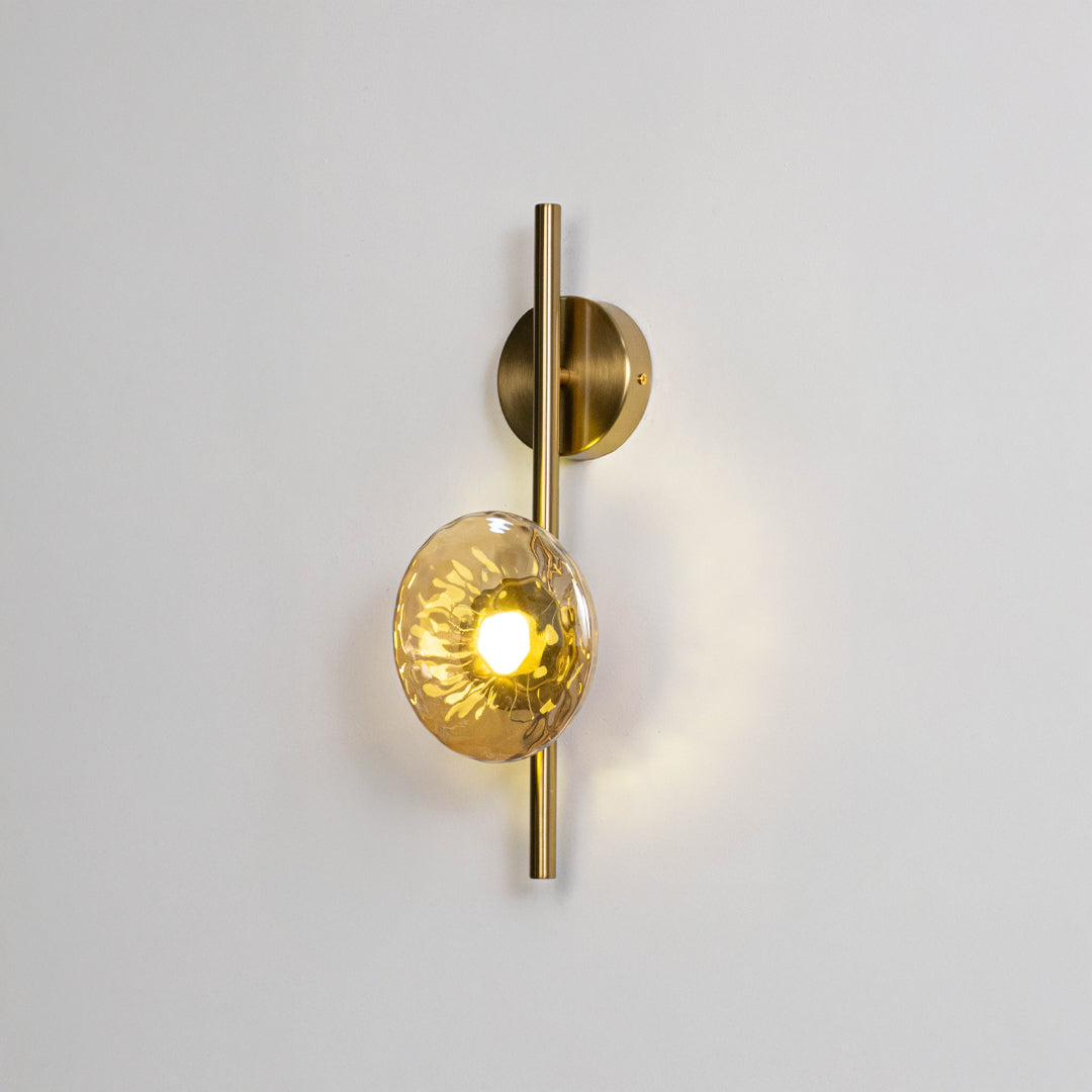 Modern wall light in gold metal finish with glass globe shade for bedroom or living room decor lighting white background.