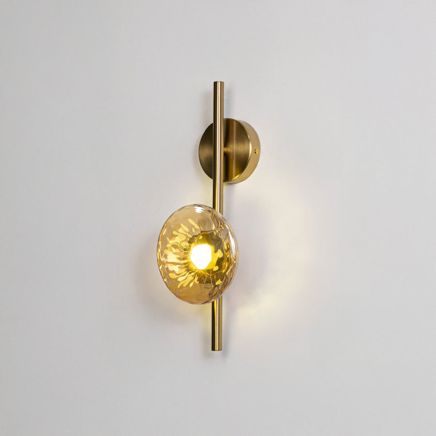 Modern wall light in gold metal finish with glass globe shade for bedroom or living room decor lighting white background.