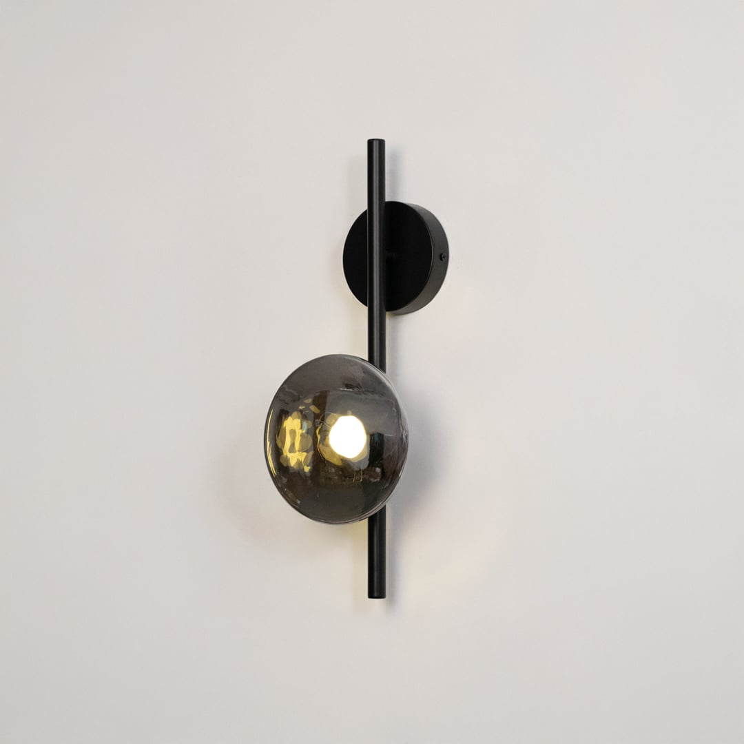 Black wall light with smoked textured glass shade illuminated on a bright white background for clear visibility.