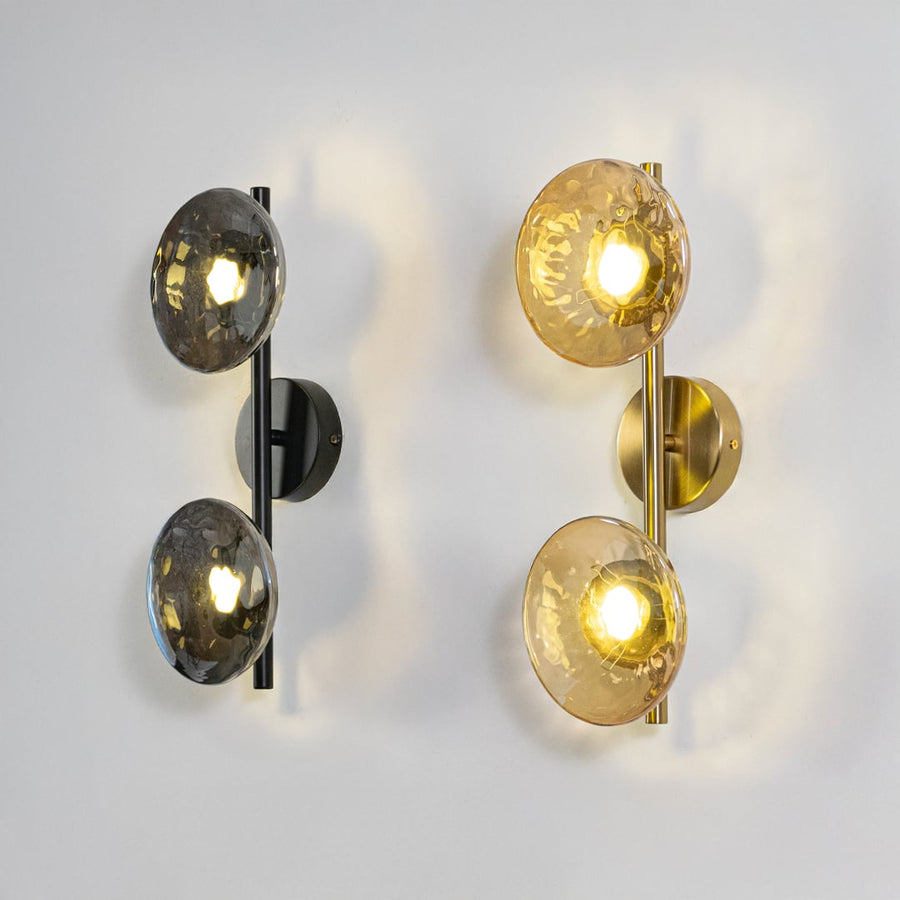 Gold double wall lights with amber textured glass globes illuminated on a clean white background showing warm glow.