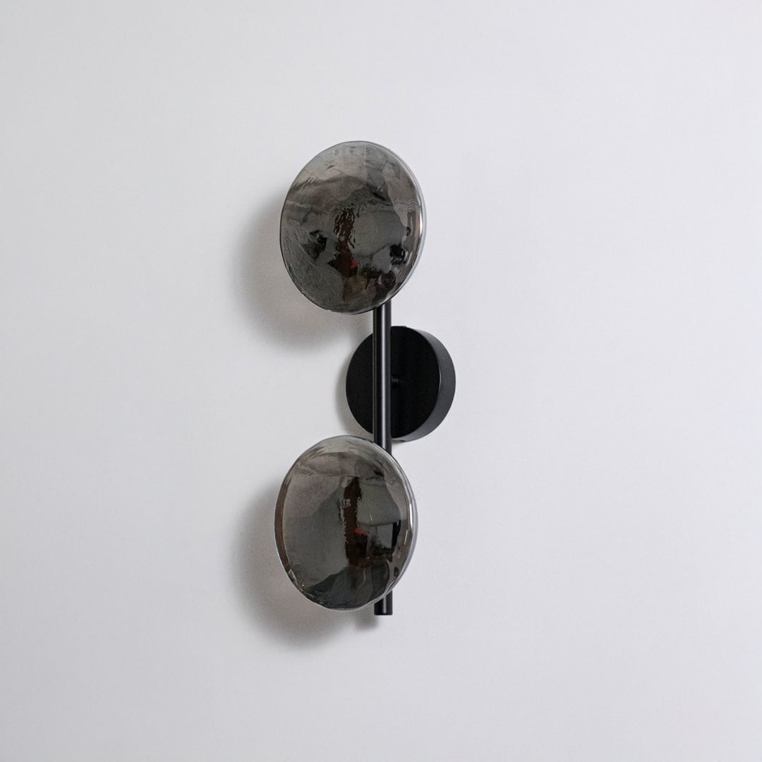 Contemporary black metal dual globe wall light fixture with smoked glass shades turned off on clean white background.