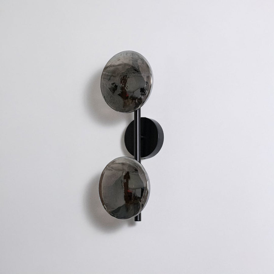 Contemporary black metal dual globe wall light fixture with smoked glass shades turned off on clean white background.
