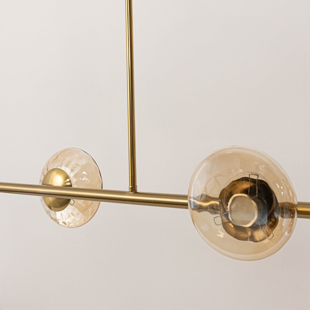 Closeup of golden metal chandelier showing amber glass shades and sleek rod detailing for designer modern ceiling decor.