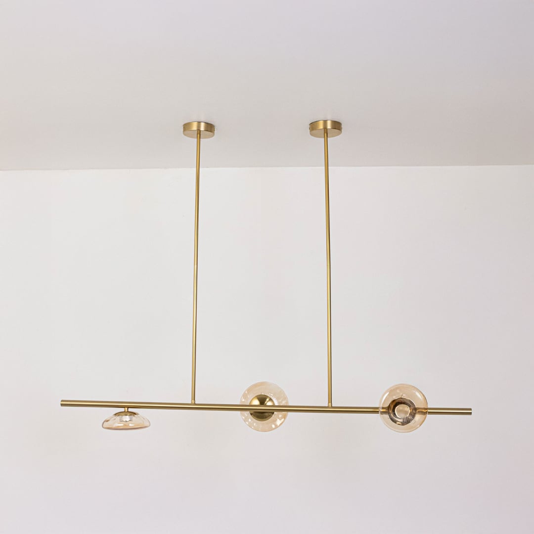 Golden metal linear chandelier with amber glass discs displayed off on white background for sophisticated modern home design.