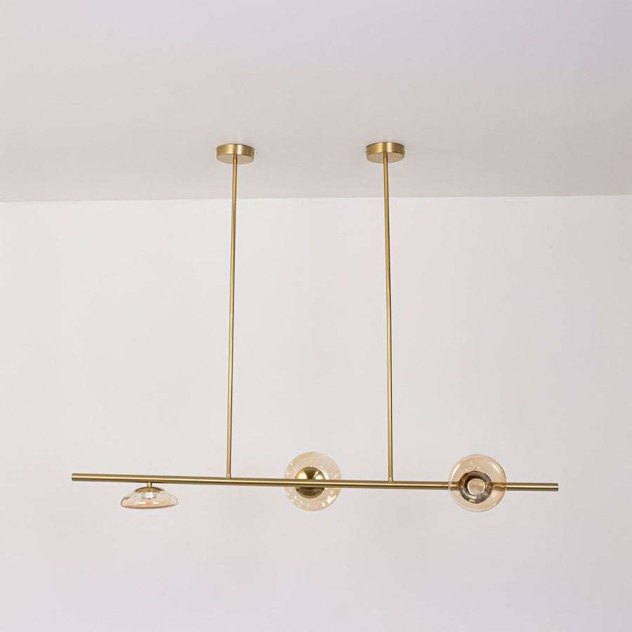 Golden metal linear chandelier with amber glass discs displayed off on white background for sophisticated modern home design.