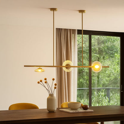 Golden metal linear chandelier with amber glass shades illuminating dining area for elegant and modern luxury home decor.