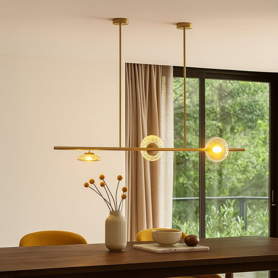 Golden metal linear chandelier with amber glass shades illuminating dining area for elegant and modern luxury home decor.
