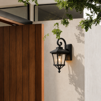 Classic black iron scroll arm tapered glass wall lantern fixture on white stucco facade for elegant porch home lighting.