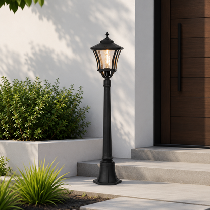 A black outdoor garden lamp post with a lit warm-white lantern, positioned on concrete steps in front of a white stucco wall and dark wood front door.