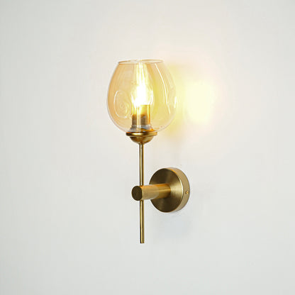 Contemporary brass wall light with amber glass globe for elegant bedroom and hallway decor.