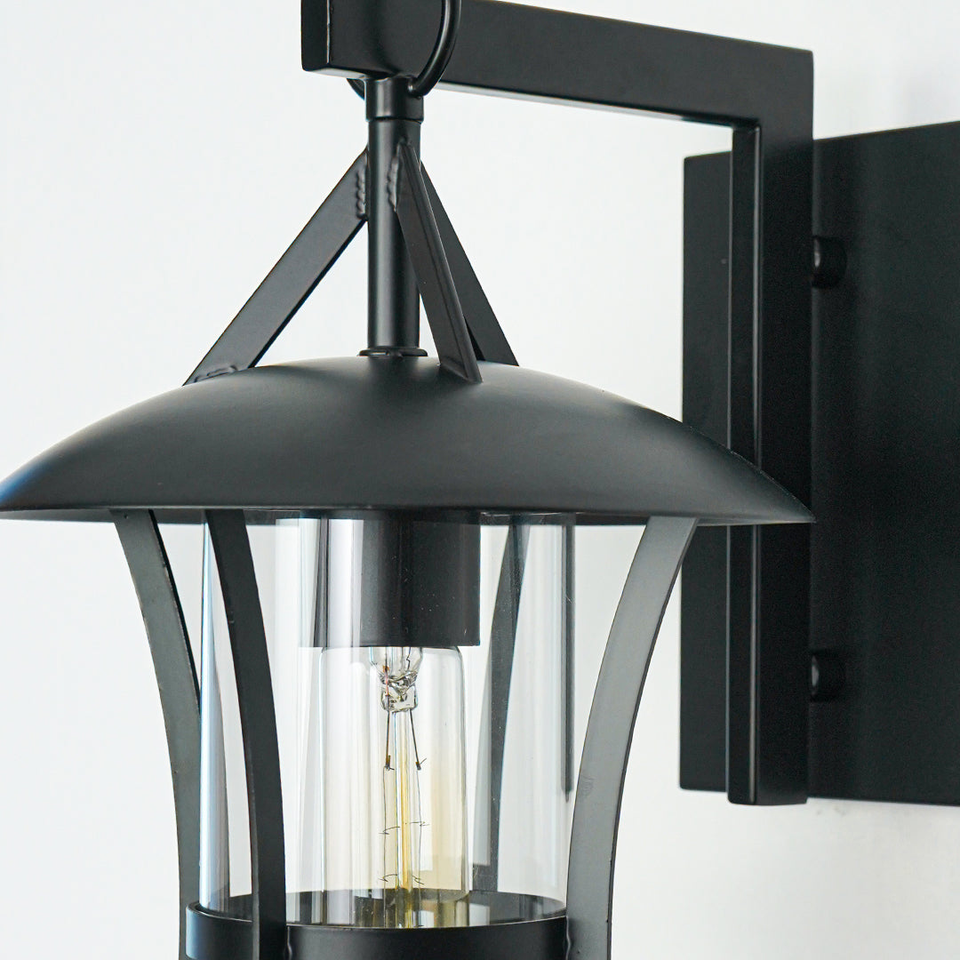 Close view of black metal wall lantern with curved arm and clear glass shade showcasing durable outdoor lighting design on neutral background.
