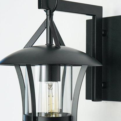 Close view of black metal wall lantern with curved arm and clear glass shade showcasing durable outdoor lighting design on neutral background.