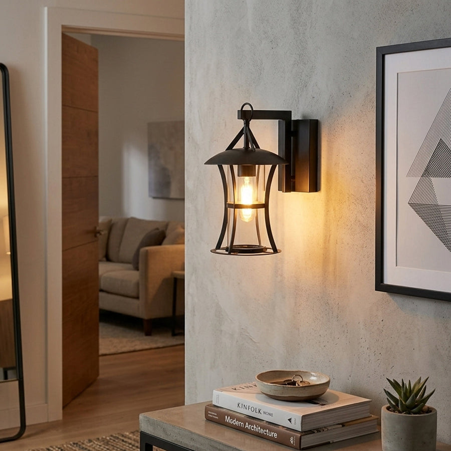 Black metal outdoor wall lantern with clear glass shade mounted near doorway on neutral wall background ideal for exterior porch or entry lighting.