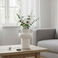 White textured ceramic decorative vase with flowers placed on wooden coffee table in modern living room interior styling.