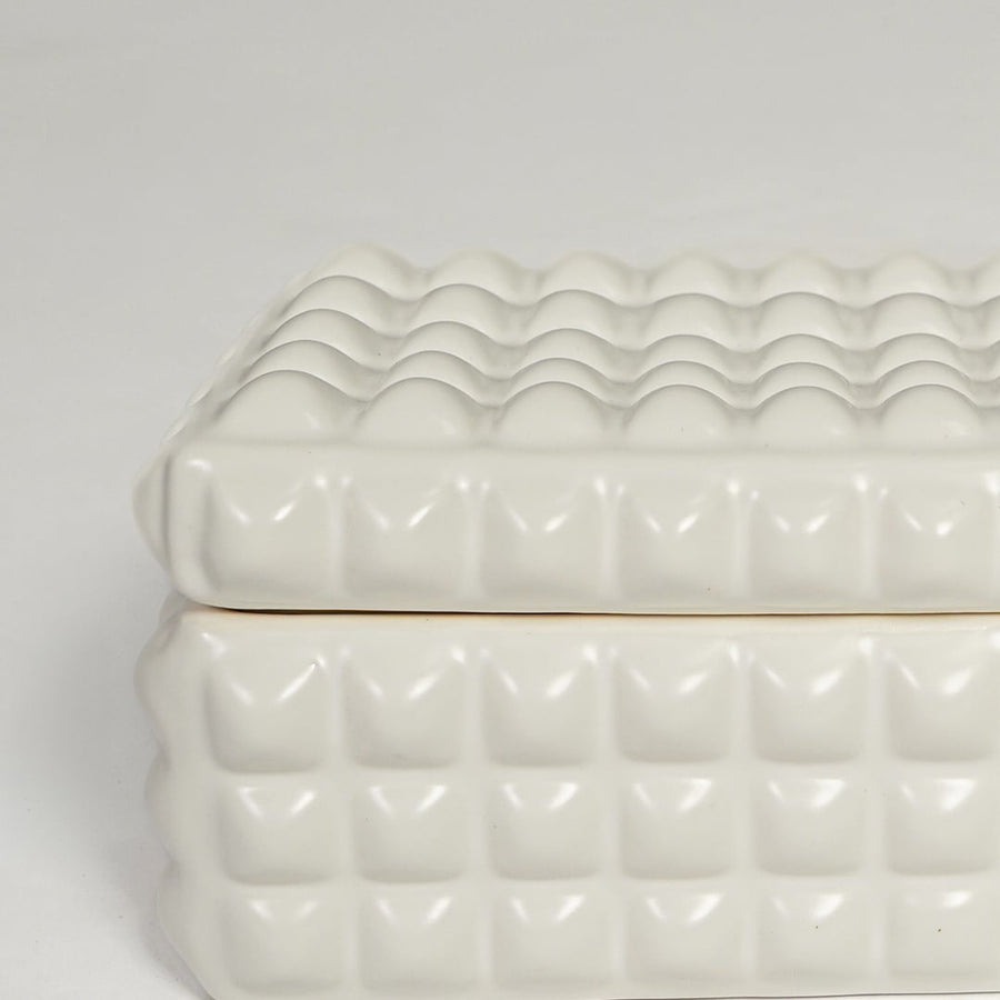 Detailed closeup of white ceramic storage box showcasing raised geometric texture and glossy finish.