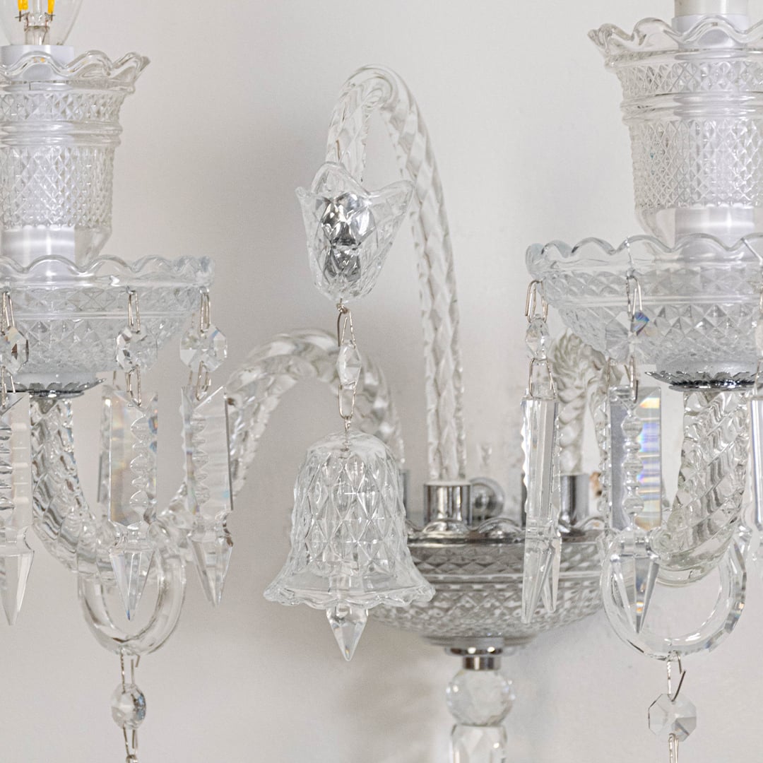 Closeup of double arm crystal wall light with ornate glass shades and hanging crystal accents for decor.