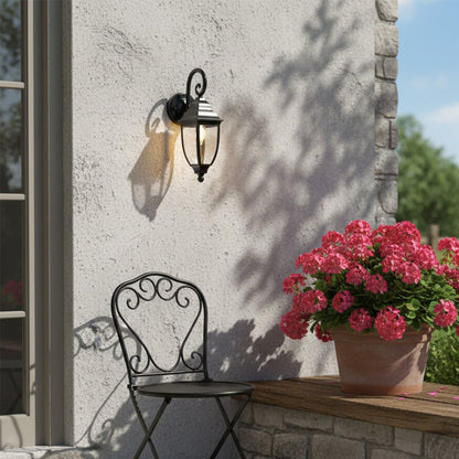 Black metal outdoor wall light lifestyle image with glass lantern shade illuminating a courtyard seating area for decor.