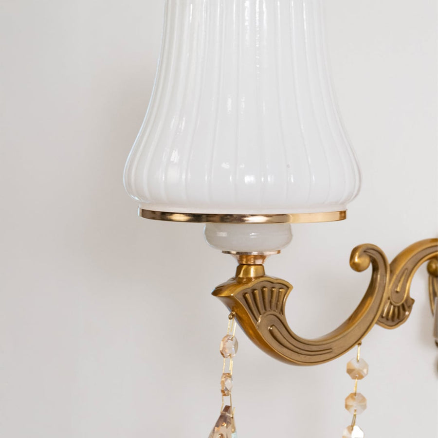 Closeup of one light crystal sconce with ornate gold base white pleated shade and hanging crystal accents.