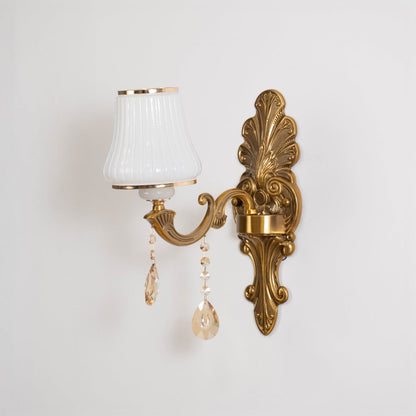 One light crystal sconce with ornate gold base and pleated white shade shown switched off on white background.