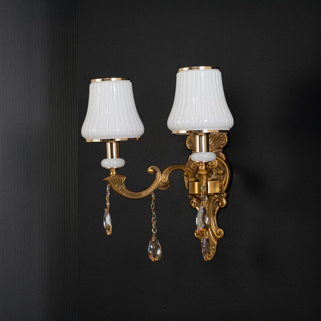 Classic two light crystal sconce with gold base and crystal drops shown switched off on black background.