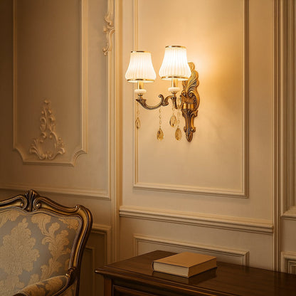 Elegant two light crystal sconce with gold base and white shades glowing warmly in classic living room decor.