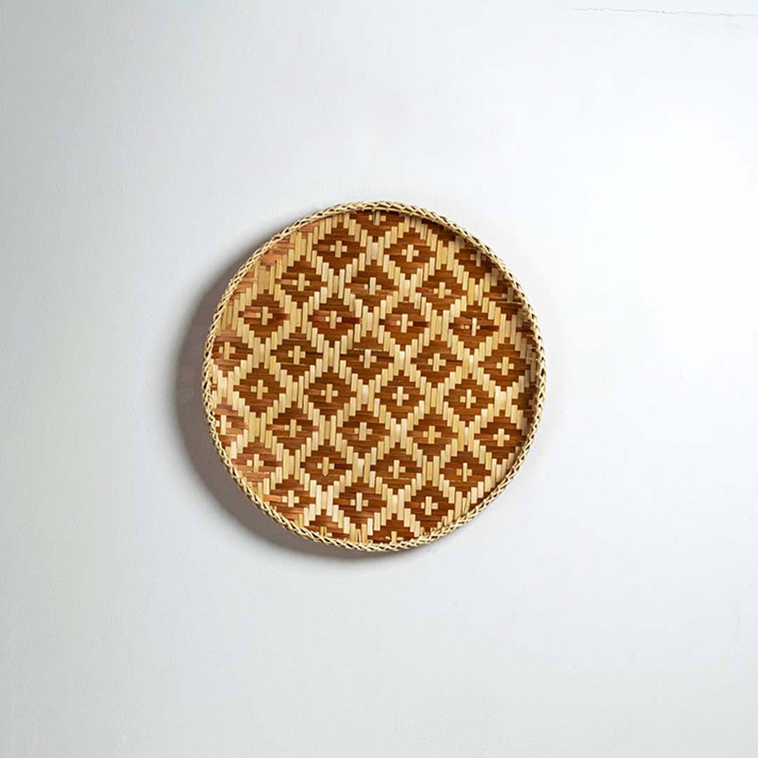 Round handcrafted brown and natural seagrass wall basket with geometric pattern on white background image.