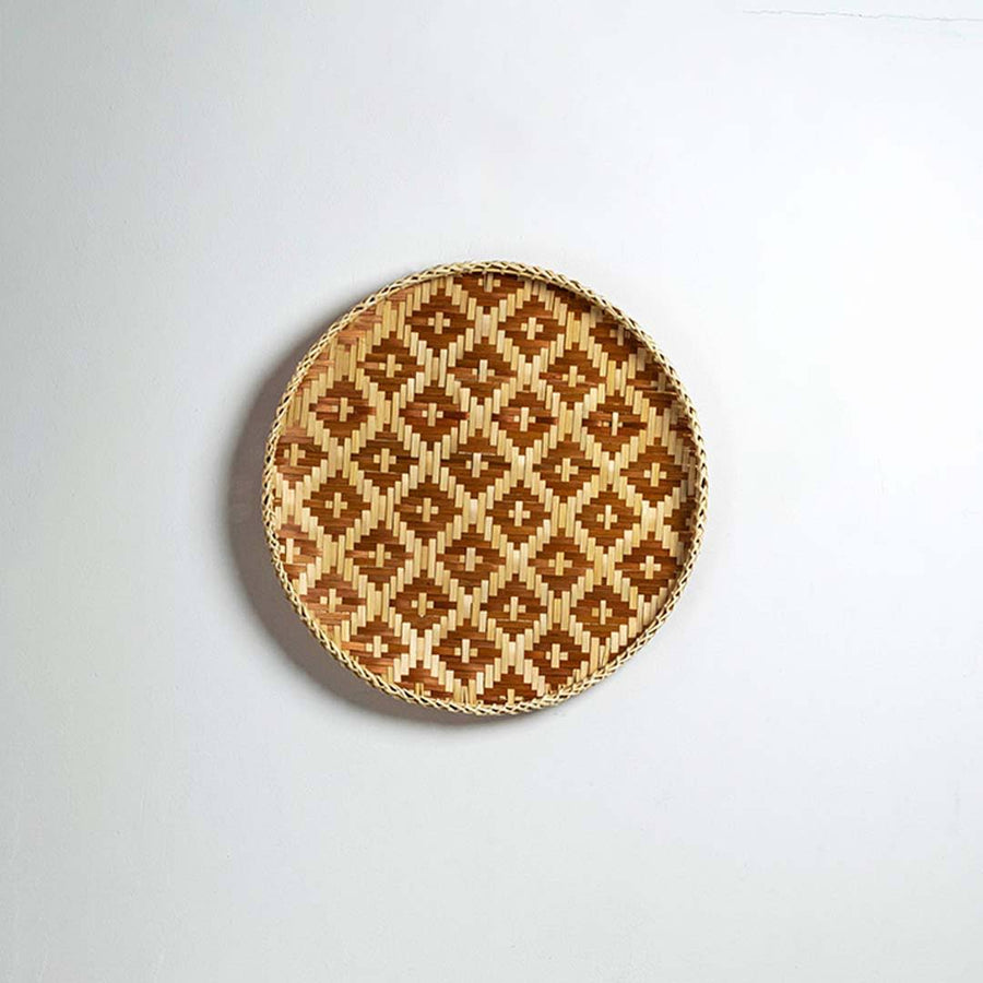 Round handcrafted brown and natural seagrass wall basket with geometric pattern on white background image.