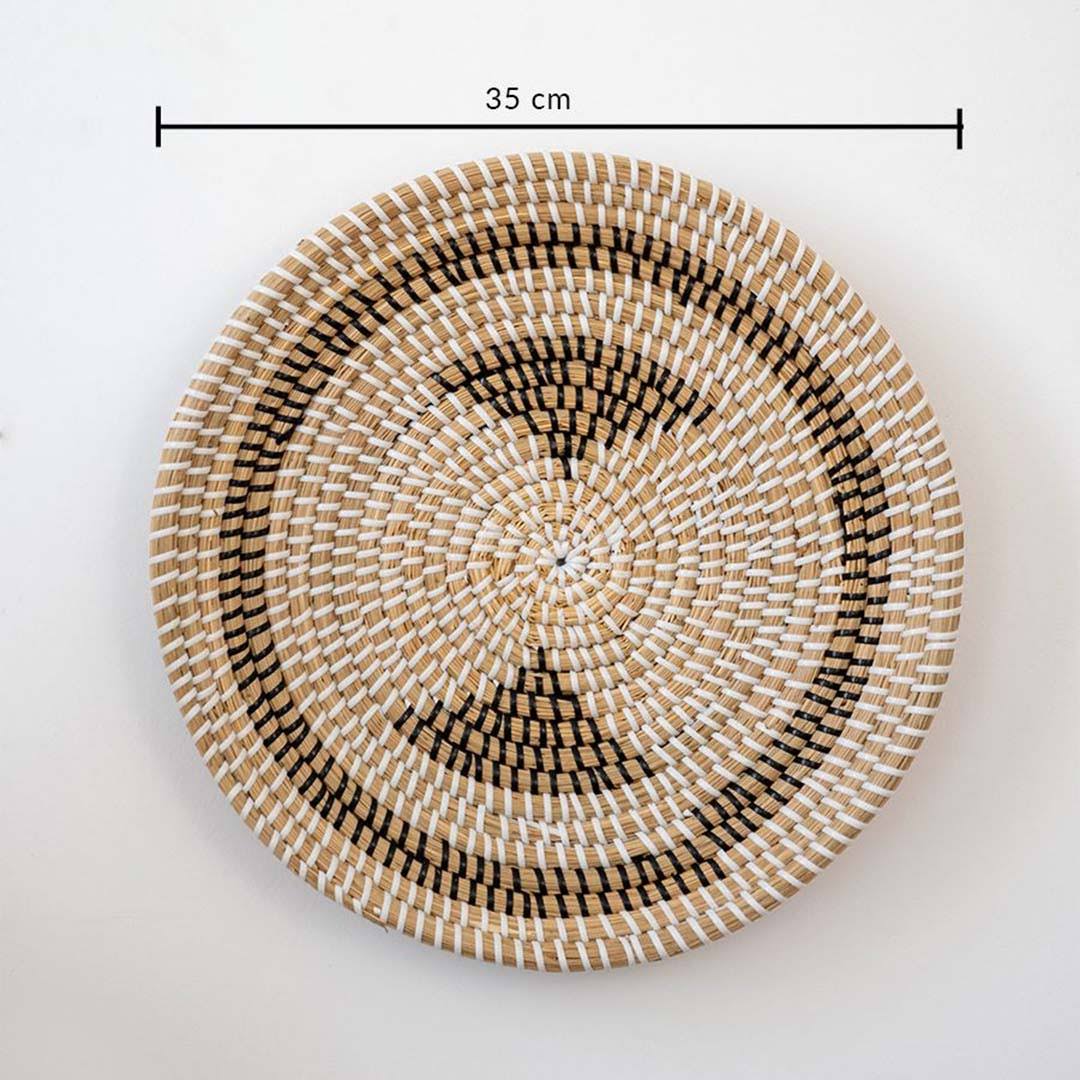 Handwoven seagrass round wall basket decor in natural beige with black crescent woven pattern displayed on white background.