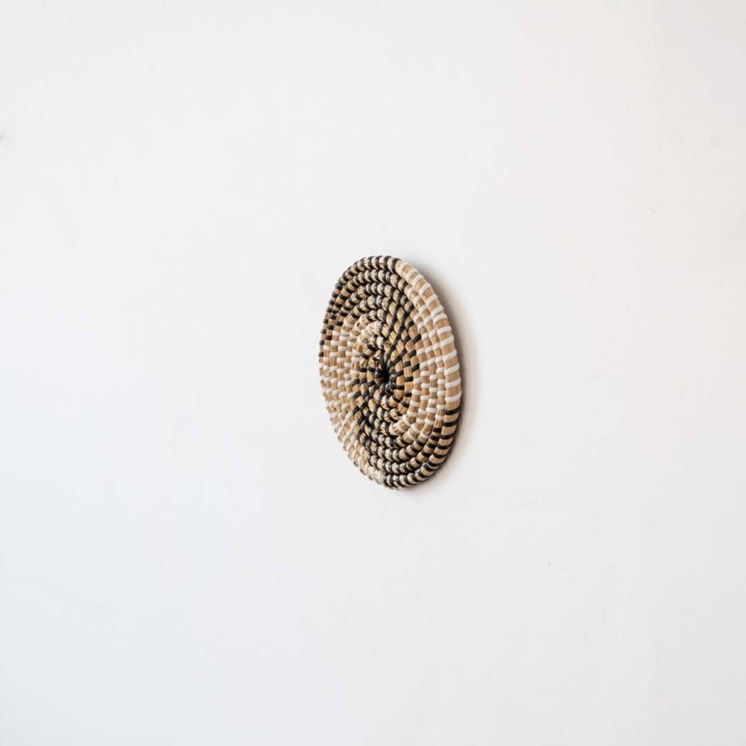 Handwoven seagrass round wall basket decor in natural beige with black spiral woven profile shown on white background.