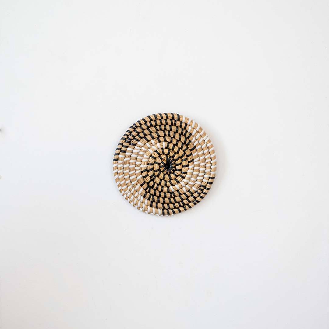Handwoven seagrass round wall basket decor in natural beige with black spiral woven pattern displayed on white background.
